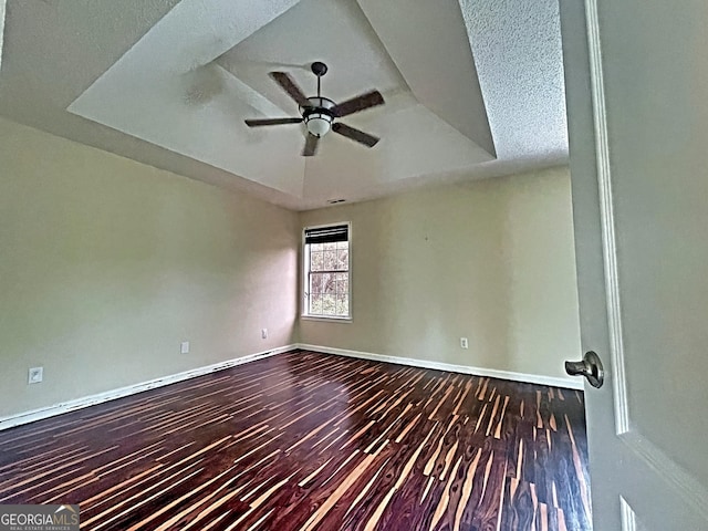 unfurnished room featuring dark wood-type flooring, ceiling fan, and a raised ceiling