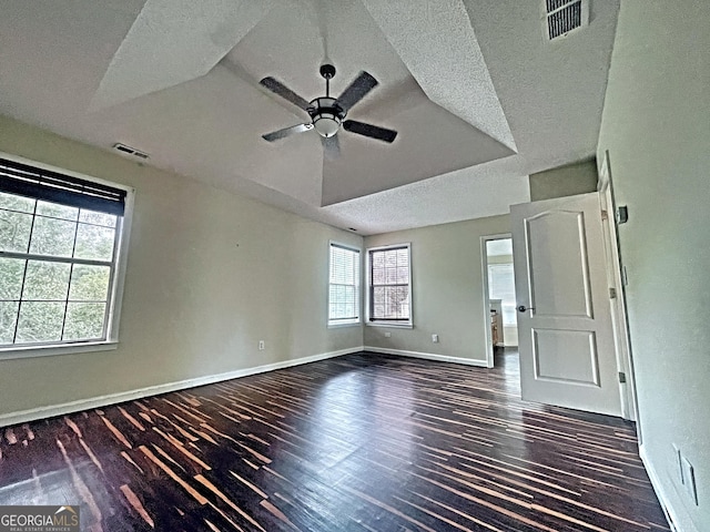 unfurnished room featuring a textured ceiling, dark wood-type flooring, a raised ceiling, and ceiling fan