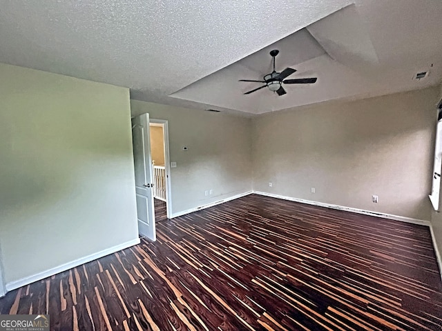 empty room with dark wood-type flooring, a textured ceiling, ceiling fan, and a tray ceiling