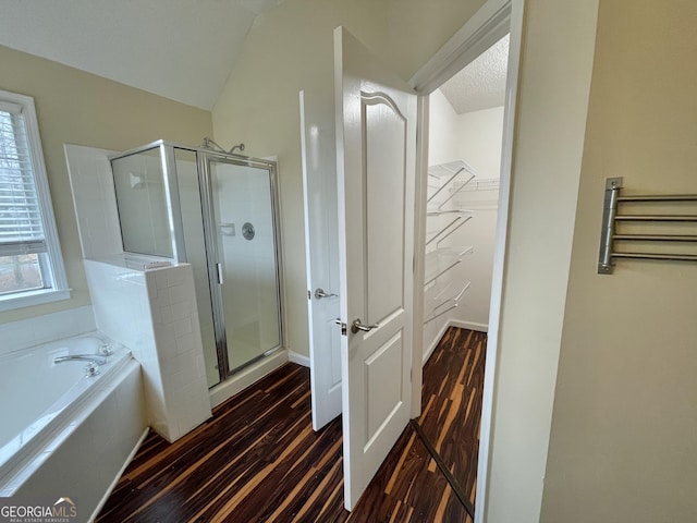 bathroom featuring a walk in closet, a shower stall, wood finished floors, baseboards, and a bath