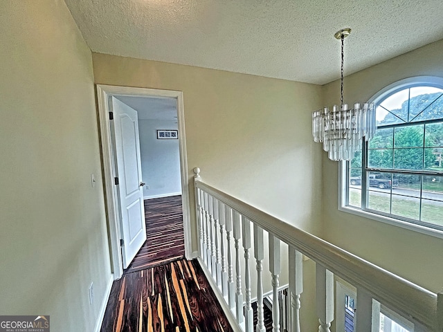 hallway with a chandelier, a textured ceiling, wood finished floors, and baseboards