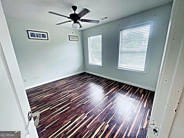 spare room featuring visible vents, dark wood finished floors, a textured ceiling, and baseboards