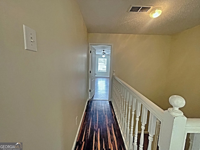 hallway with a textured ceiling, dark wood-style flooring, an upstairs landing, visible vents, and baseboards