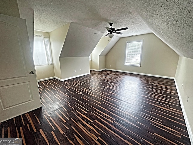 additional living space with a textured ceiling, baseboards, vaulted ceiling, and dark wood-style flooring