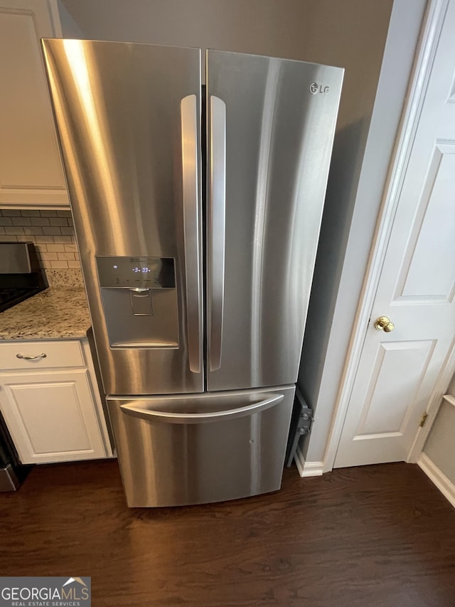 interior details with dark wood-type flooring, stainless steel fridge, light stone countertops, and white cabinets