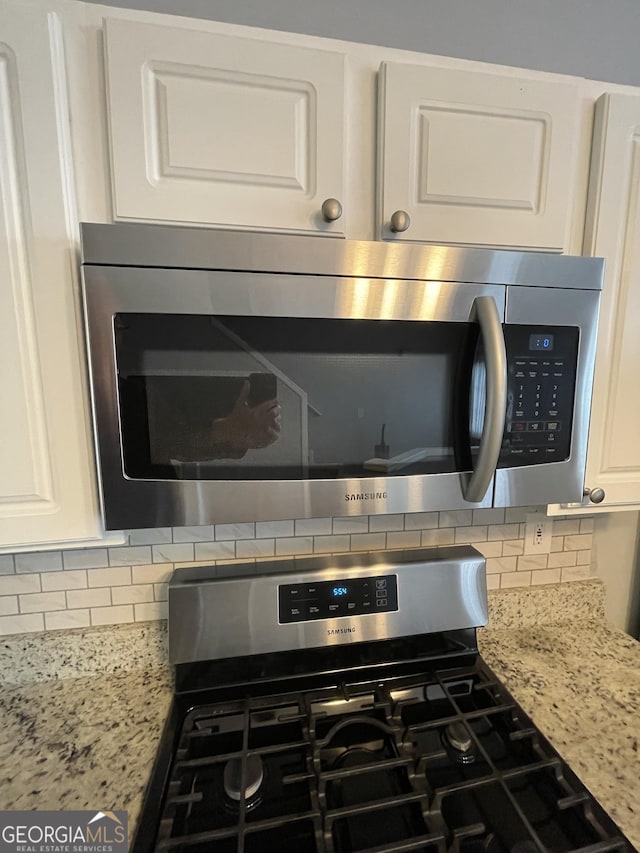 room details featuring white cabinetry, stainless steel appliances, light stone countertops, and tasteful backsplash