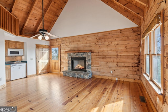 unfurnished living room with beamed ceiling, a wealth of natural light, a stone fireplace, and wood walls