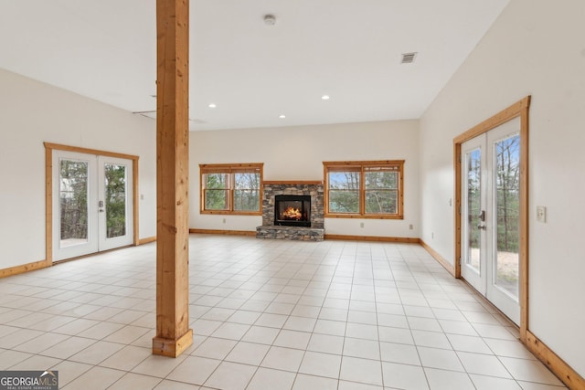 unfurnished living room with french doors, a stone fireplace, light tile patterned flooring, and a wealth of natural light