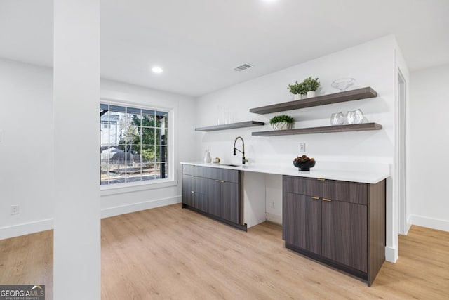 bar with dark brown cabinets, sink, and light wood-type flooring