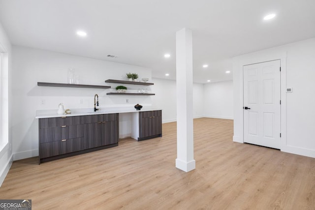 bar featuring sink, dark brown cabinets, and light hardwood / wood-style floors