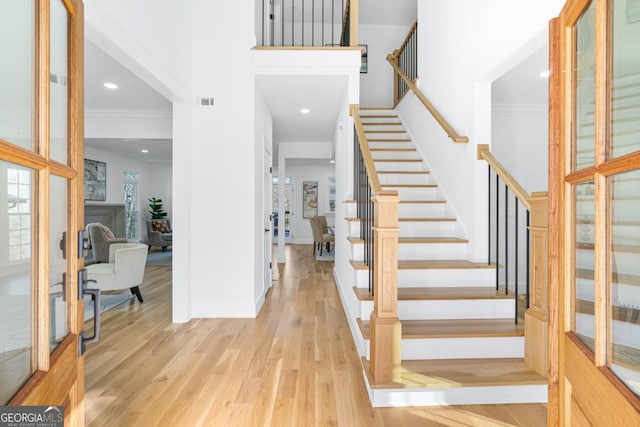 entrance foyer featuring crown molding, a towering ceiling, and light wood-type flooring