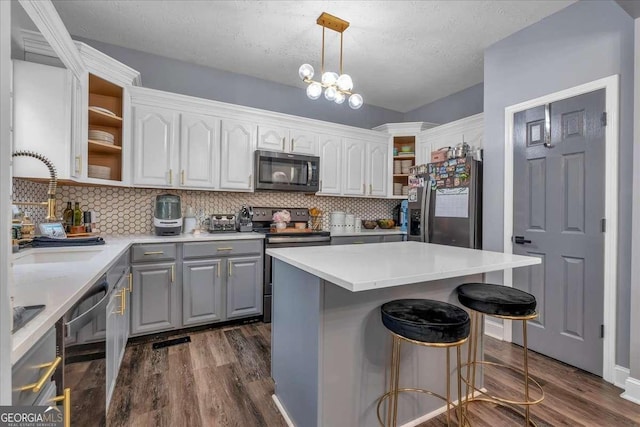 kitchen with sink, a kitchen island, pendant lighting, stainless steel appliances, and white cabinets