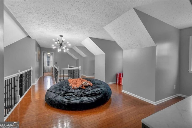 interior space featuring wood-type flooring, a chandelier, vaulted ceiling, and a textured ceiling