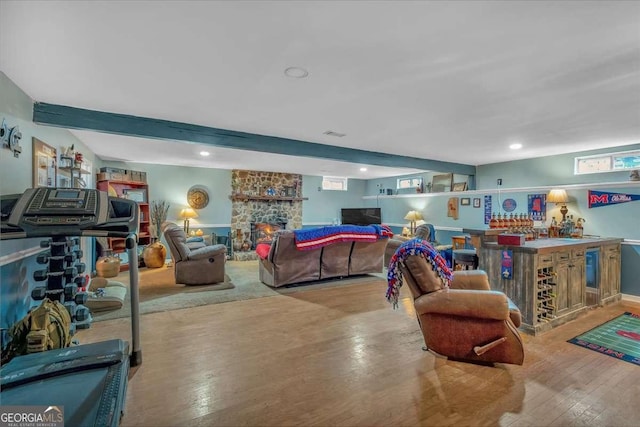 living room featuring beamed ceiling, a stone fireplace, indoor bar, and light hardwood / wood-style flooring