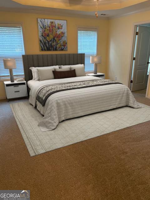 carpeted bedroom with a tray ceiling and ornamental molding