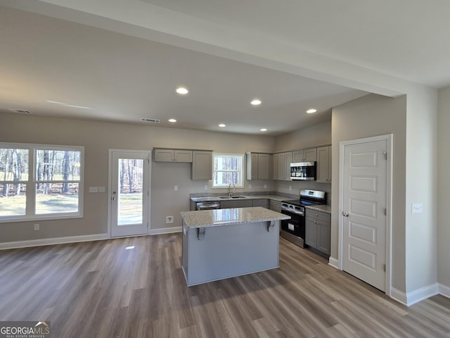 kitchen with gray cabinets, appliances with stainless steel finishes, sink, a center island, and light stone countertops