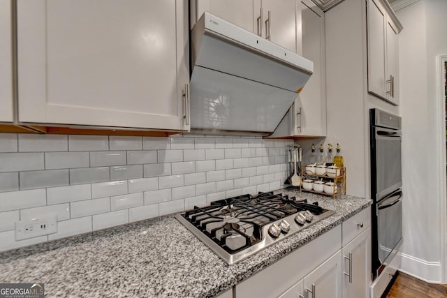 kitchen featuring extractor fan, stainless steel gas cooktop, backsplash, and light stone counters