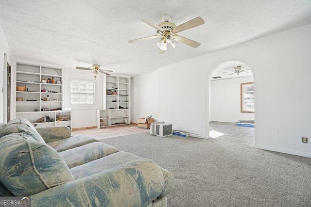 carpeted living room with ceiling fan, built in features, and a textured ceiling