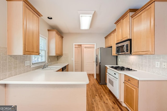 kitchen with stainless steel appliances, light brown cabinetry, kitchen peninsula, and sink