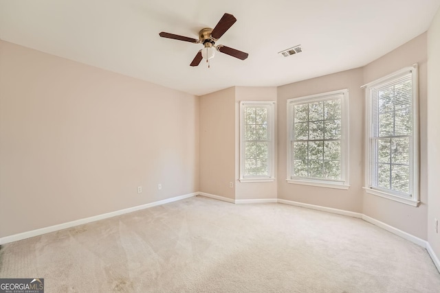 spare room featuring light carpet, a wealth of natural light, and ceiling fan