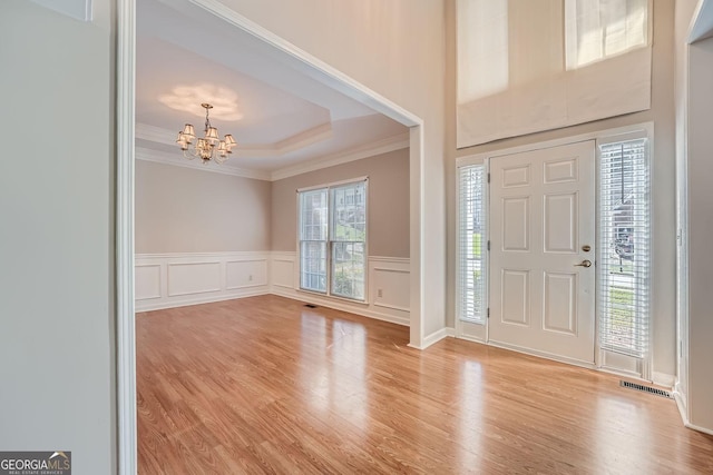 entrance foyer with ornamental molding, a raised ceiling, light wood-type flooring, and a notable chandelier