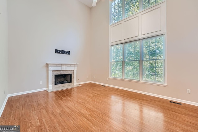 unfurnished living room featuring a towering ceiling, a premium fireplace, and light hardwood / wood-style floors