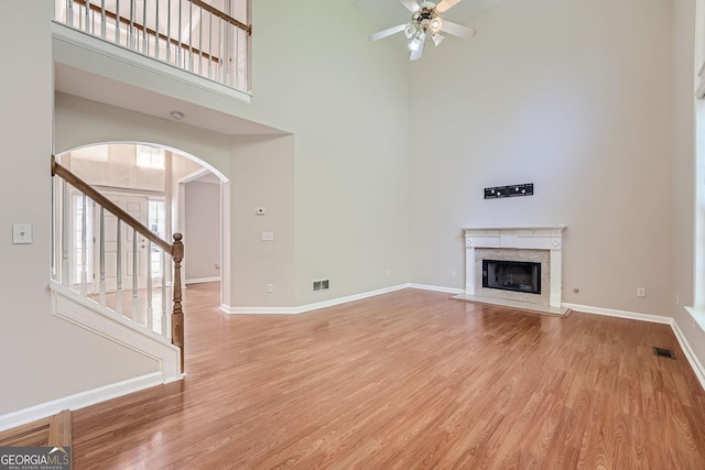 unfurnished living room with a high ceiling, a premium fireplace, ceiling fan, and light wood-type flooring