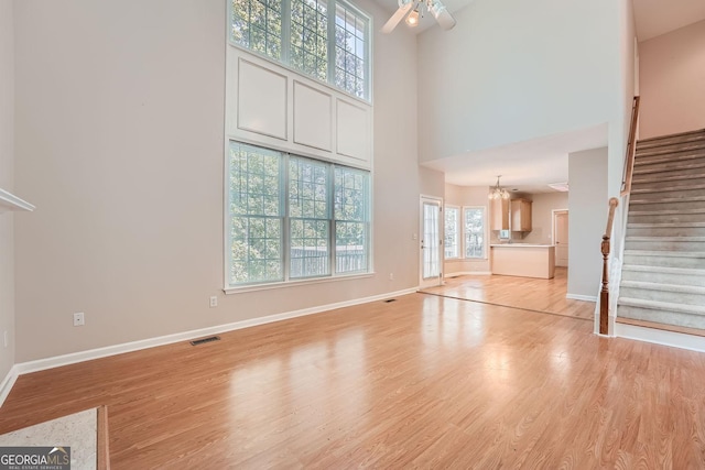 unfurnished living room with a towering ceiling, ceiling fan with notable chandelier, and light hardwood / wood-style flooring