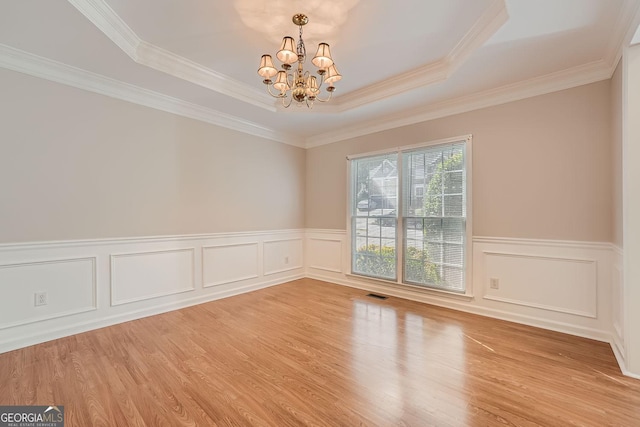 spare room with a notable chandelier, light hardwood / wood-style flooring, ornamental molding, and a raised ceiling