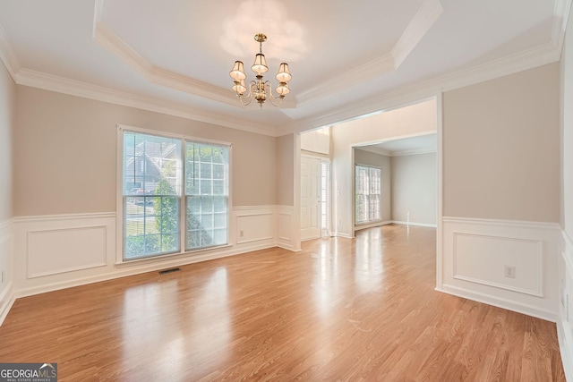 empty room featuring crown molding, a notable chandelier, light hardwood / wood-style floors, and a tray ceiling