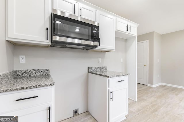 kitchen with white cabinetry, light stone countertops, and light hardwood / wood-style floors