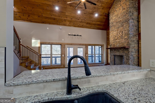 kitchen with a stone fireplace, sink, high vaulted ceiling, wooden ceiling, and light stone countertops