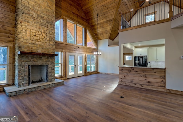 unfurnished living room with a stone fireplace, dark wood-type flooring, high vaulted ceiling, and french doors