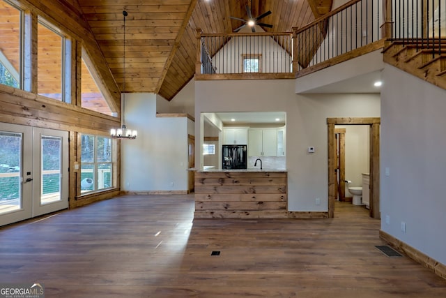 unfurnished living room with high vaulted ceiling, ceiling fan with notable chandelier, dark wood-type flooring, and wooden ceiling