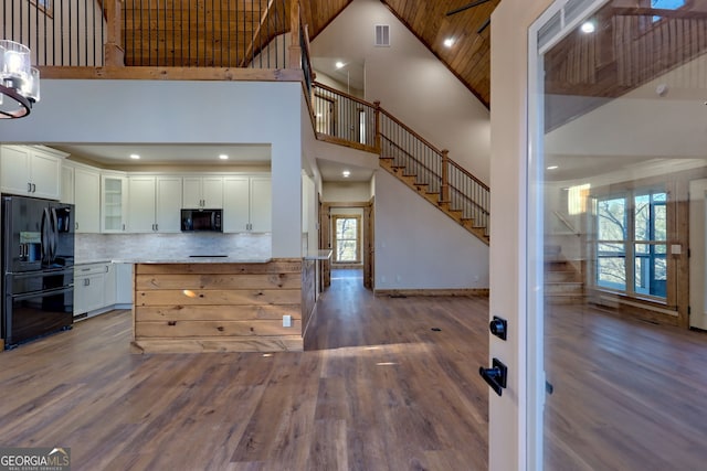 kitchen with white cabinetry, tasteful backsplash, black appliances, hardwood / wood-style flooring, and a high ceiling