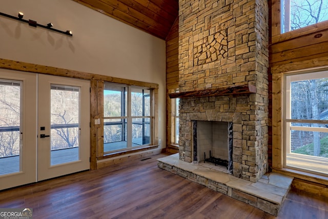 unfurnished living room featuring hardwood / wood-style flooring, high vaulted ceiling, a stone fireplace, wooden ceiling, and french doors