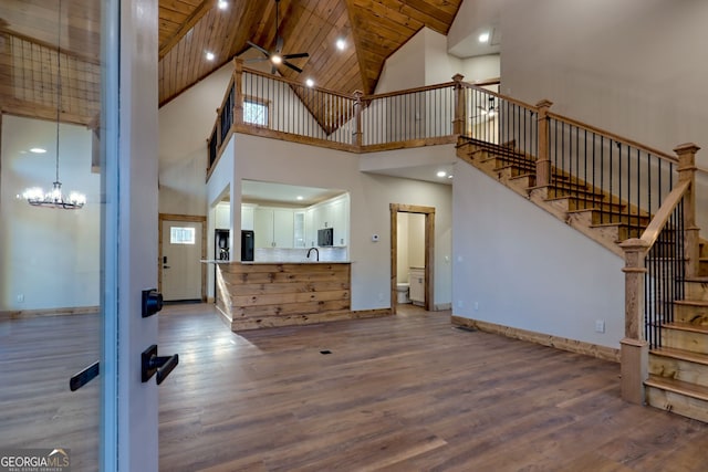 unfurnished living room with sink, wood ceiling, ceiling fan with notable chandelier, and light wood-type flooring