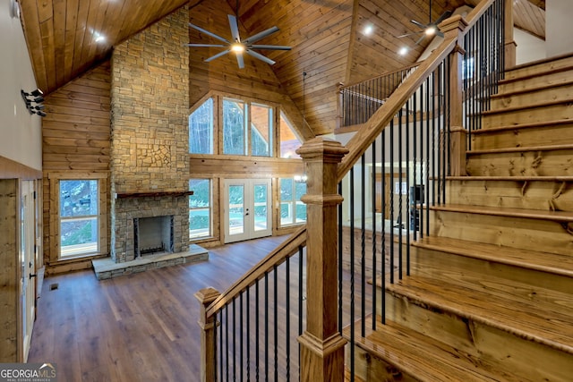 staircase with high vaulted ceiling, wooden ceiling, ceiling fan, a fireplace, and hardwood / wood-style floors