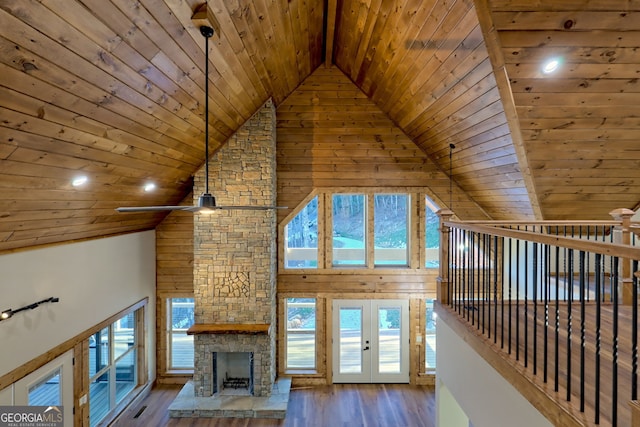 unfurnished living room with hardwood / wood-style floors, high vaulted ceiling, a stone fireplace, wooden ceiling, and french doors