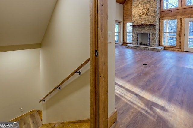 stairway featuring a stone fireplace, high vaulted ceiling, and hardwood / wood-style floors