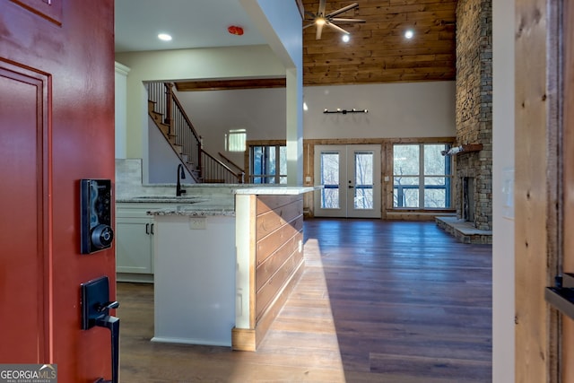 interior space featuring sink, dark wood-type flooring, a towering ceiling, a stone fireplace, and french doors