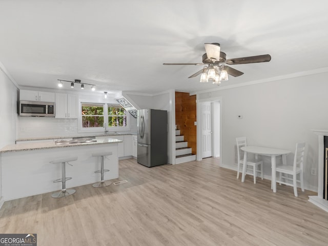 kitchen featuring a breakfast bar area, appliances with stainless steel finishes, ornamental molding, light stone countertops, and white cabinets