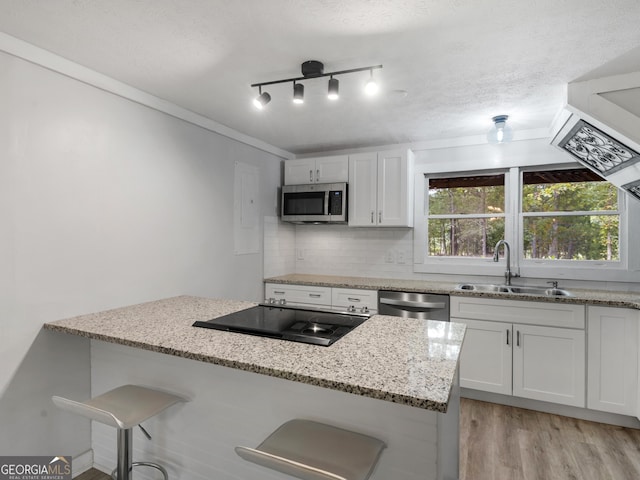 kitchen with sink, a breakfast bar, white cabinetry, stainless steel appliances, and light stone counters