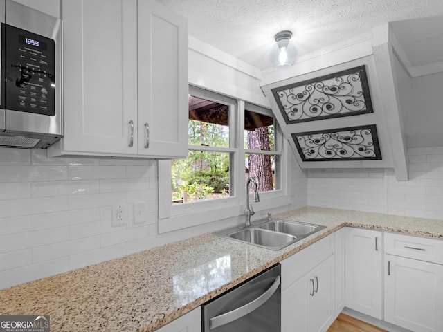 kitchen with sink, appliances with stainless steel finishes, white cabinetry, light stone countertops, and decorative backsplash