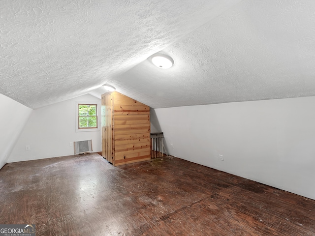 additional living space featuring vaulted ceiling, dark hardwood / wood-style floors, and a textured ceiling