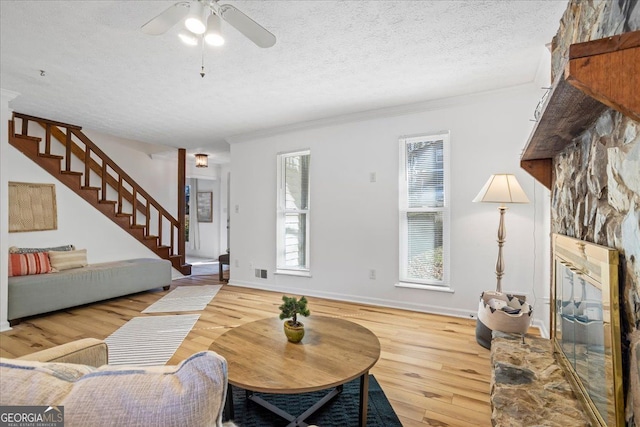 living room featuring crown molding, a textured ceiling, ceiling fan, a fireplace, and light hardwood / wood-style floors