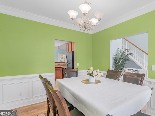 dining area featuring ornamental molding, sink, a notable chandelier, and light wood-type flooring