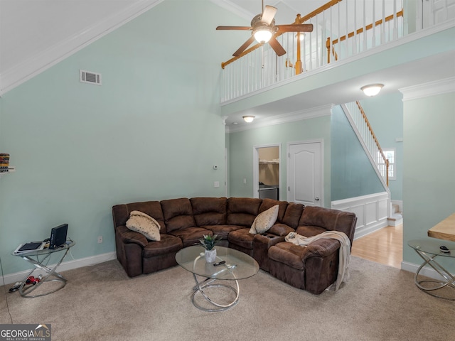 living room featuring ceiling fan, a towering ceiling, ornamental molding, and light carpet