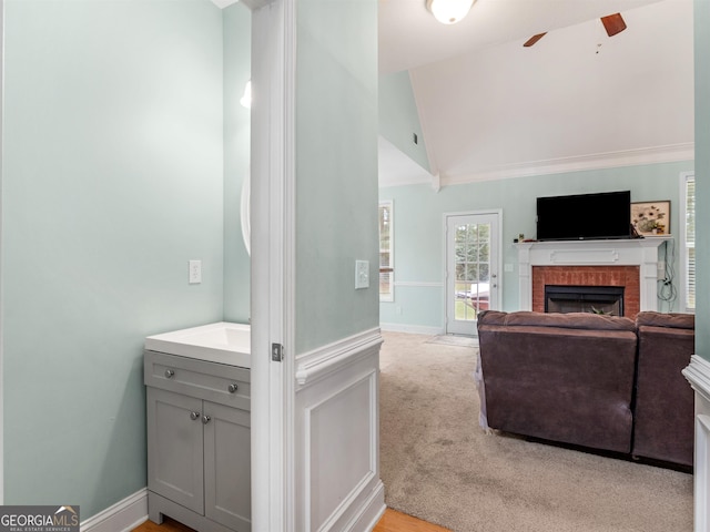 interior space featuring vaulted ceiling, a brick fireplace, light colored carpet, and ceiling fan