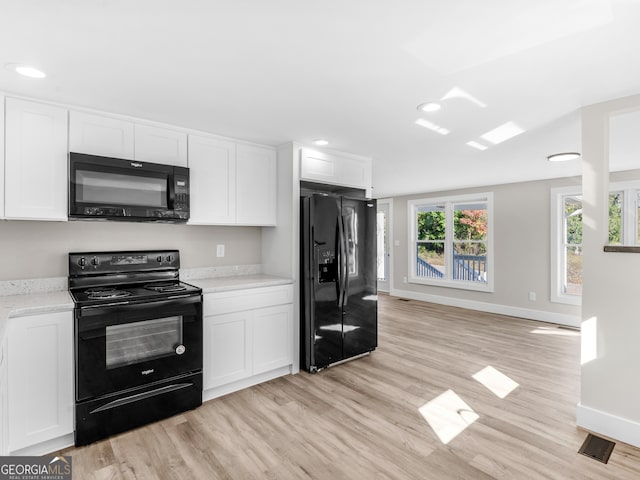 kitchen featuring white cabinetry, light stone counters, black appliances, and light wood-type flooring